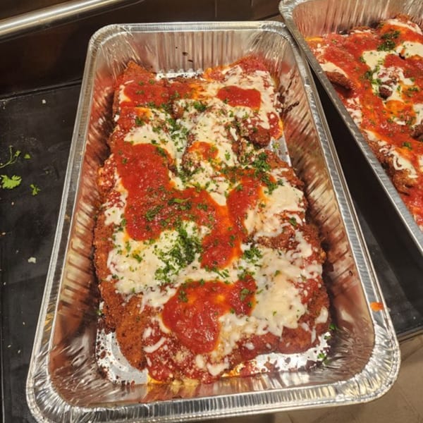 Two foil pans filled with Stallone's Italian Eatery's chicken parmesan, topped with sauce, cheese, and parsley.