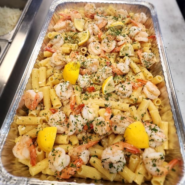 A catering tray filled with Stallone's Italian Eatery's shrimp scampi pasta, garnished with lemon and parsley.