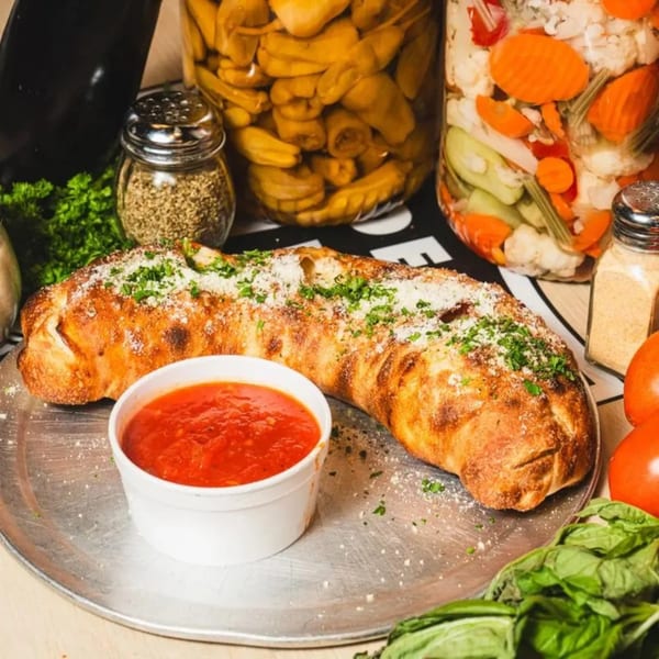 A golden-brown calzone with parmesan and parsley, served with a side of marinara sauce.