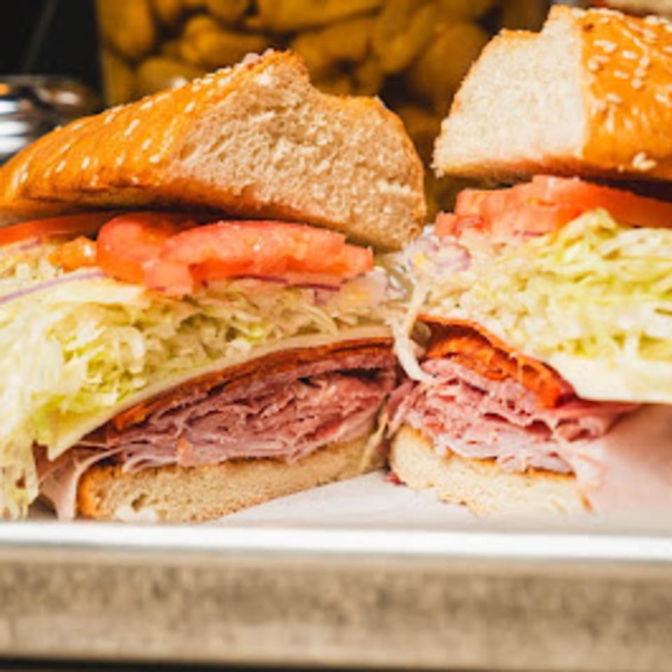 Two halves of a large Italian sub sandwich with various meats, cheese, lettuce, and tomatoes.