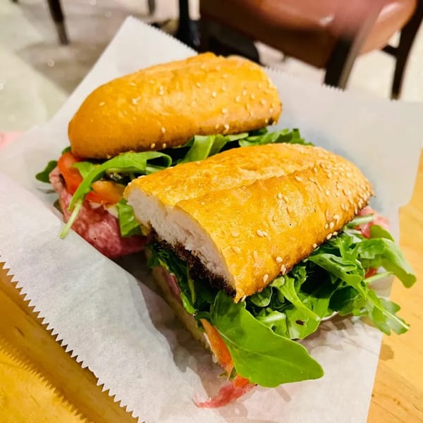 A Stallone's Italian Eatery Italian sub sandwich, with salami, arugula, and tomatoes on a sesame seed bun.