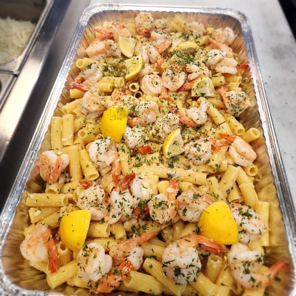 A catering tray of Stallone's Italian Eatery's shrimp pasta with lemon wedges and parsley.