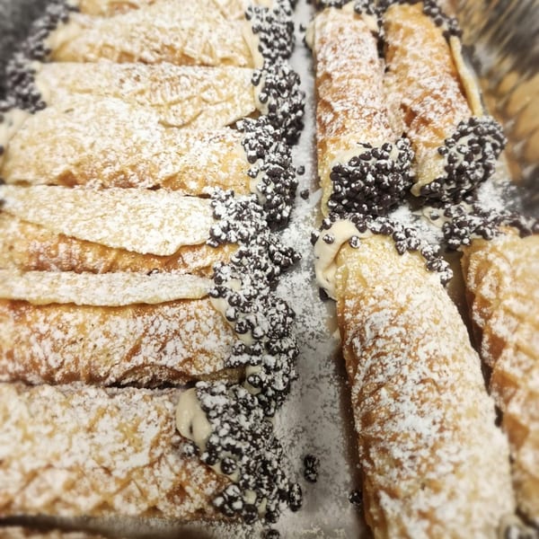 Rows of Stallone's Italian Eatery cannolis, dusted with powdered sugar and chocolate chips.
