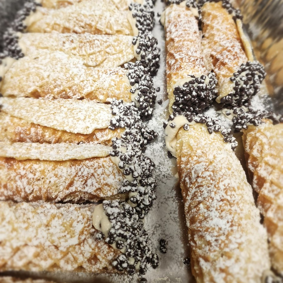 Rows of Stallone's Italian Eatery cannolis, dusted with powdered sugar and chocolate chips.