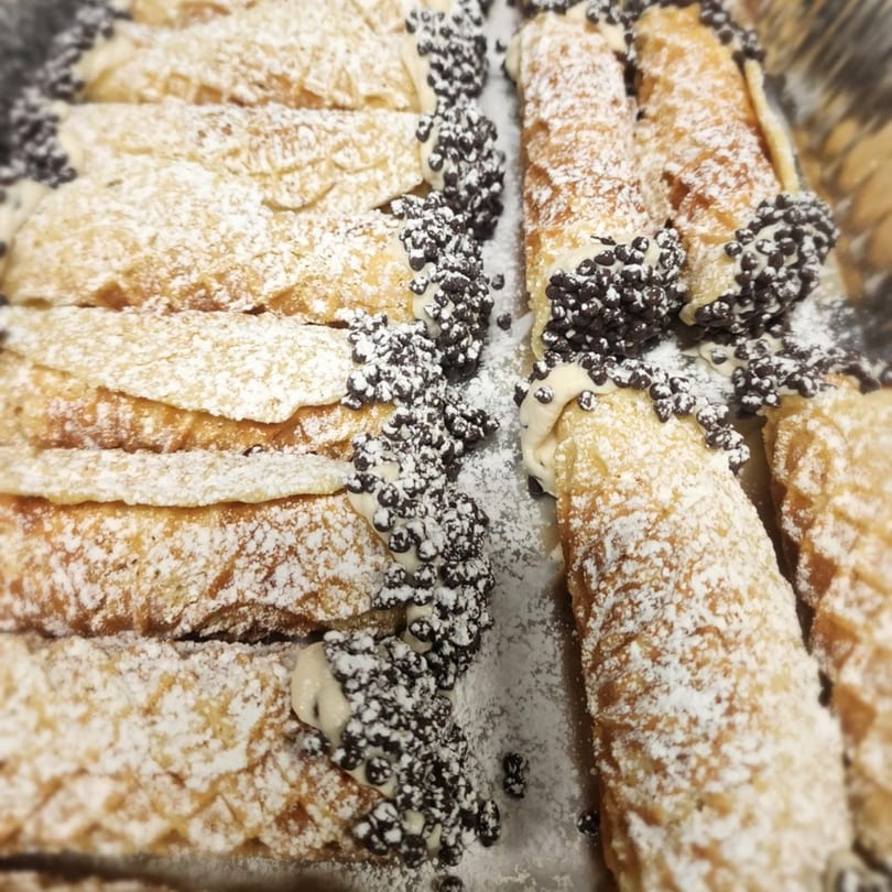 Rows of Stallone's Italian Eatery cannolis, dusted with powdered sugar and chocolate chips.